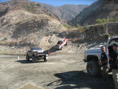 1987 Ford Bronco - Off-road vehicles navigate a challenging dirt incline under a clear sky.