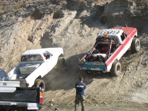 1987 Ford Bronco - Off-road vehicles navigate a challenging dirt incline, kicking up dust as they ascend.