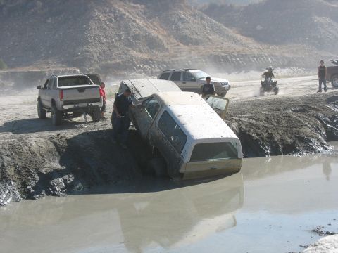 1987 Ford Bronco - Several vehicles are stuck in a muddy off-road area, with one Bronco partially submerged.