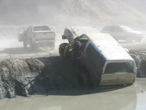 1987 Ford Bronco - Multiple off-road vehicles are stuck in a muddy pit, with one vehicle's hood open.