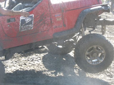 1987 Ford Bronco - A red Jeep Wrangler is shown off-road, displaying a USPS logo and a veteran sticker on its door.