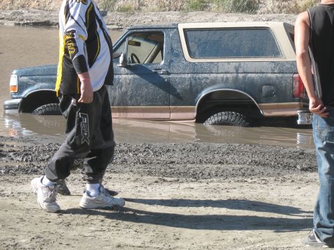 1987 Ford Bronco - A Ford Bronco is stuck in a muddy puddle, with two people observing the situation.