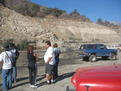 1987 Ford Bronco - A blue Ford Bronco is parked on a dirt area with a rocky hillside behind it the background.