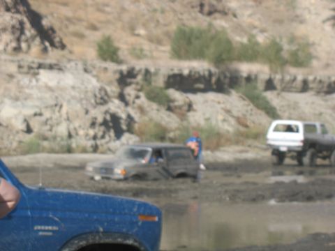 1987 Ford Bronco - Multiple SUVs, including a 1987 Ford Bronco, navigate a muddy off-road course.
