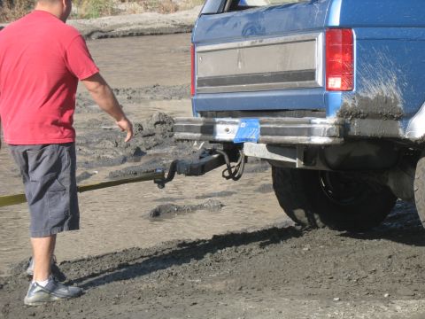 1987 Ford Bronco - Man pulls a blue 1987 Ford Bronco from mud with a strap attached to the hitch.