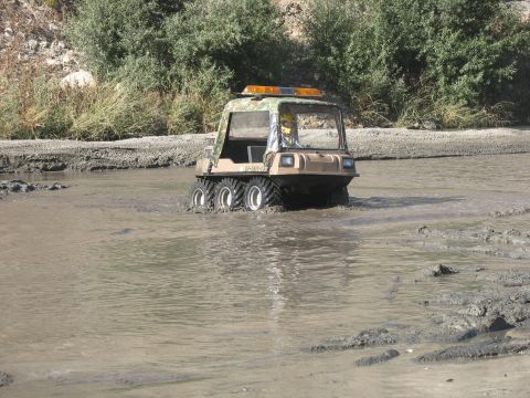 1987 Ford Bronco - An amphibious vehicle navigates through a muddy, watery terrain with trees in the background.