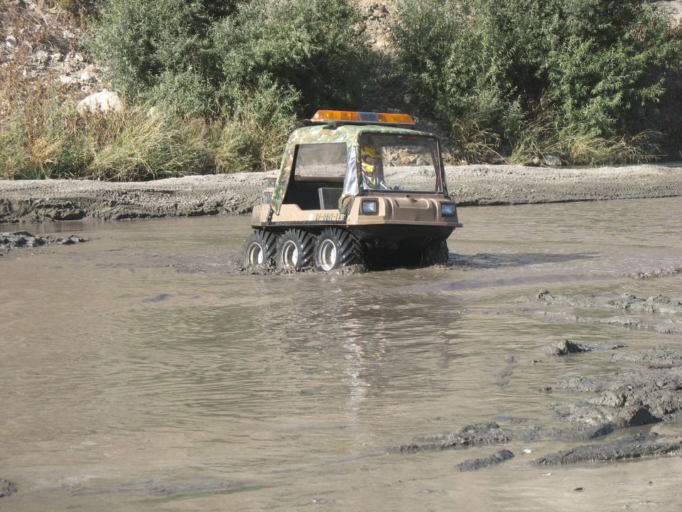 Tan amphibious vehicle with camouflage pattern on top, driving through muddy water