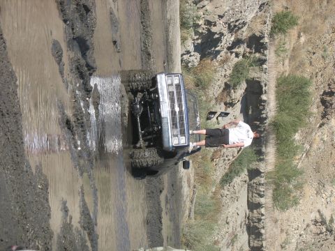 1987 Ford Bronco - A man stands beside a silver truck stuck in a muddy off-road trail.