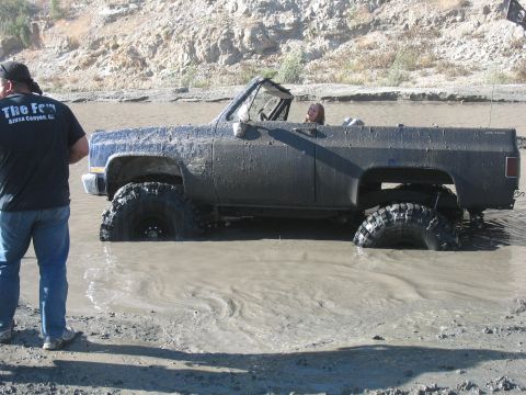 1987 Ford Bronco - This SUV is deeply stuck in the mud, with only its tires and lower body visible. A person watches from the side.