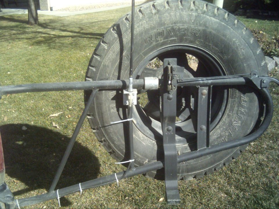 Swing-out spare tire carrier with Dunlop tire and antenna mount, shown against a grass lawn
