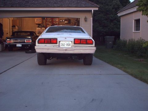 1978 Ford Mustang II - A white sedan is parked in a driveway, with a black car visible inside an open garage.