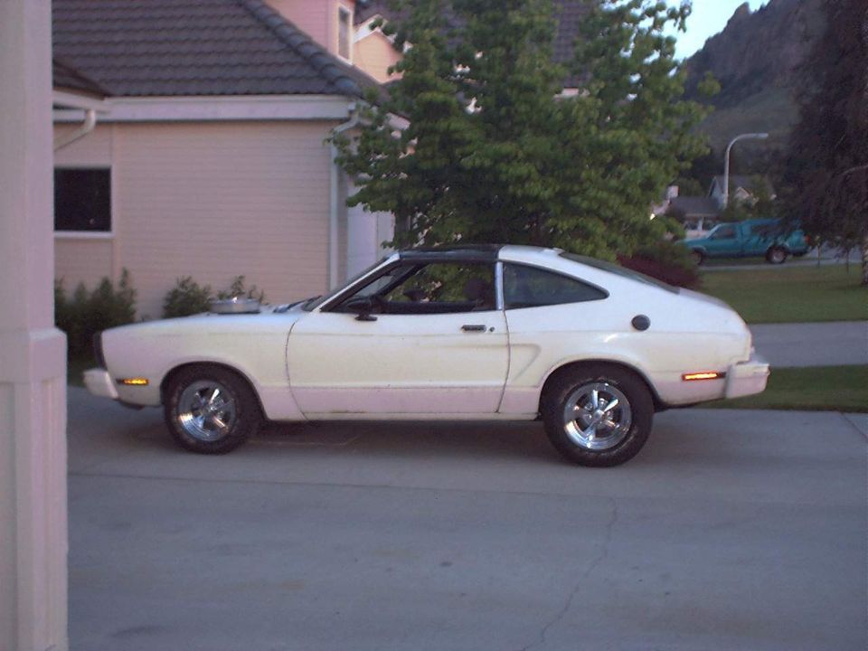 White Mustang II hatchback in profile on a driveway at dusk with polished mag wheels