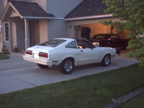1978 Ford Mustang II - A white 1978 Ford Mustang II coupe with a black vinyl roof is parked in a driveway, with another car visible in the garage behind it.