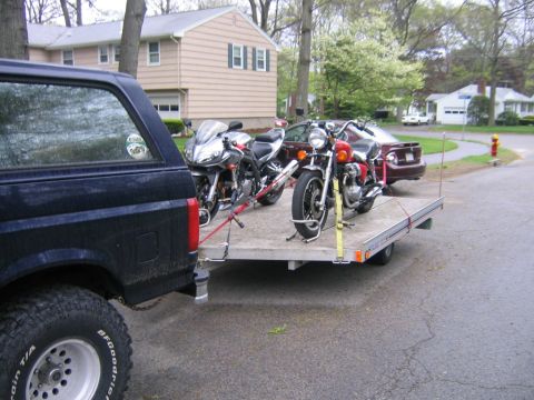 1994 Ford Bronco - 1994 Ford Bronco hauling two motorcycles on a trailer down a suburban street.