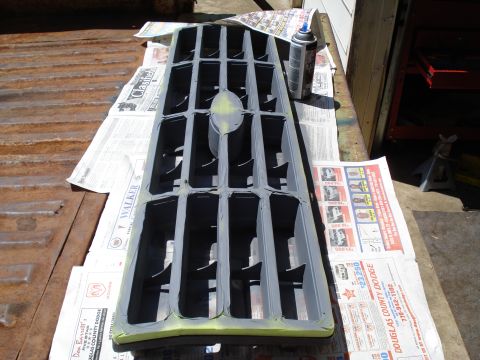 1984 Ford Bronco - A vehicle grille is covered in primer and ready for a new coat of paint, laid out on a surface covered with old newspapers.