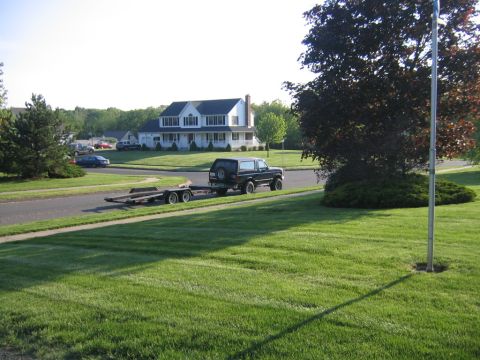 1994 Ford Bronco - A black SUV tows a trailer down a residential street past a large white house.