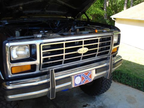 1984 Ford Bronco - Front view of a Ford truck's grille and bumper, with the hood open.
