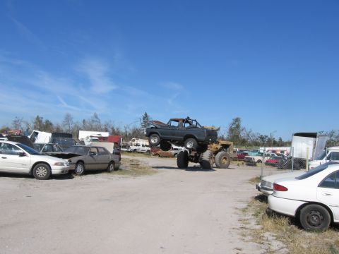 1995 Ford F-150 - A modified 1995 Ford F-150 pickup truck is displayed precariously on top of a large monster truck chassis in a junkyard setting.