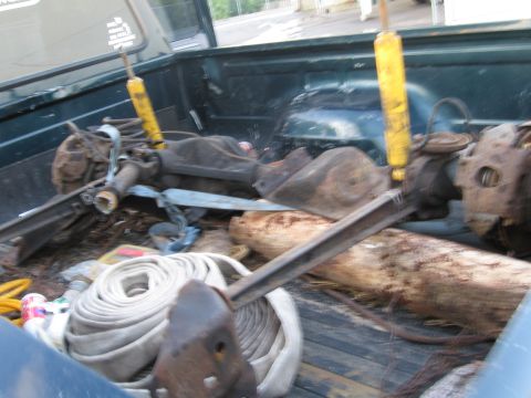 1995 Ford F-150 - Pickup truck bed contains disassembled vehicle parts and equipment, including axles and shocks.