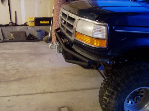 1995 Ford Bronco - Front view of a dark blue Ford Bronco with an aftermarket bumper and winch, revealing its grille and headlight assembly.