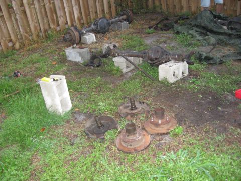 1995 Ford F-150 - Two front axle assemblies and four hubs are laid out on the grass near a wooden fence.