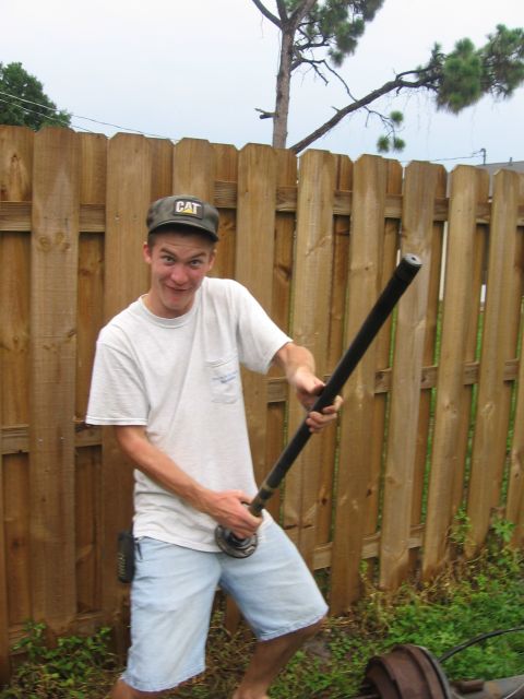 1995 Ford F-150 - A man poses with a pipe in front of a wooden fence, wearing a CAT hat and denim shorts.