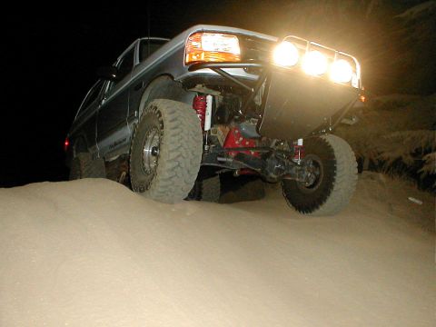 1996 Ford Bronco - Modified Ford Bronco navigates a sandy dune at night with auxiliary lights illuminating the path.