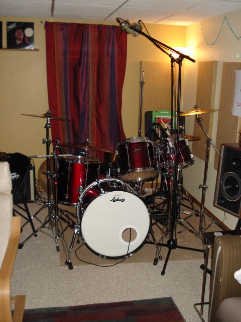 1986 Ford Bronco - A red drum kit is set up in a room, likely a studio, with soundproofing panels on the wall and a microphone overhead.