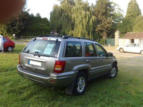 1991 Ford Crown Victoria - A silver Jeep Grand Cherokee is parked on a grassy area with trees and a building in the background.
