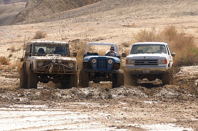 White Ford Bronco with custom bumper and lights driving through mud, 3/4 front view