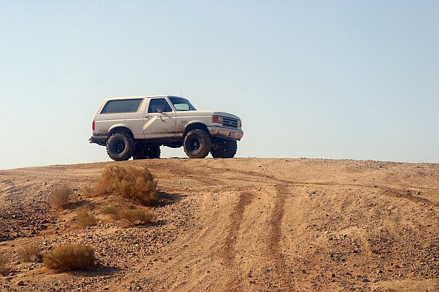 White Ford Bronco on a dirt hill, lifted suspension, off-road tires, clear sky