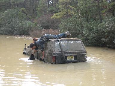 1989 Jeep Cherokee - A person attempts to free a Jeep Cherokee submerged in murky water, with trees and foliage in the background.