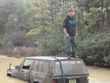 1989 Jeep Cherokee - A man stands on the roof of a muddy 1989 Jeep Cherokee stuck in a waterlogged area.