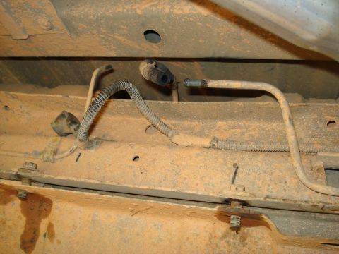 1984 Ford Bronco - Close-up view of the underbody fuel lines and wiring harness, showing corrugated tubing and metal lines.
