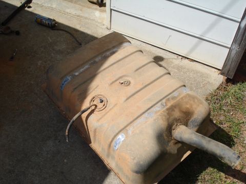 1984 Ford Bronco - A rusty fuel tank sits on concrete next to a white garage door, with a can of spray paint nearby.