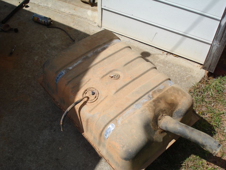Rusty metal fuel tank with hoses and a can of spray paint on concrete
