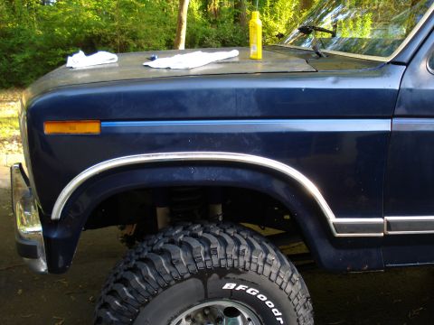 1984 Ford Bronco - A blue SUV's fender, tire, and hood are shown, with cleaning supplies on the hood.
