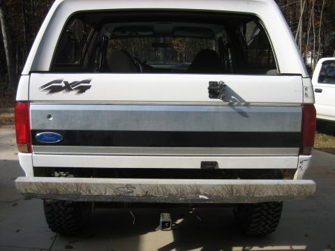 1996 Ford Bronco - Straight-on rear view of a white full-size Ford Bronco with the rear glass retracted, showing the tailgate with its silver/black trim band,…