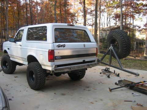 1996 Ford Bronco - White two-door Ford Bronco SUV shown from the rear three-quarter angle, lifted on large mud-terrain tires with black wheels, '4x4' badging…