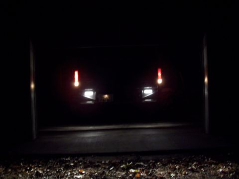 1983 Ford Bronco - A dark SUV is parked inside a garage at night, its lights illuminating the space.