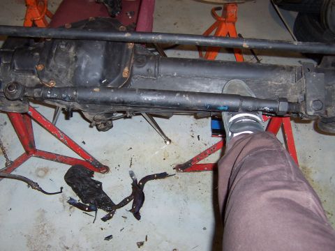 1990 Ford Bronco - A vehicle's front axle assembly is supported by jack stands, with a person's foot visible near the steering components.