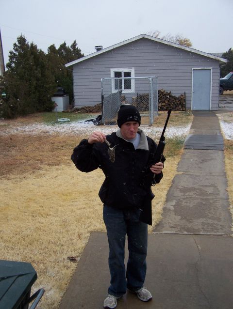 1995 Ford Bronco - Man with hunting rifle and squirrel stands outside a house during a snowfall.