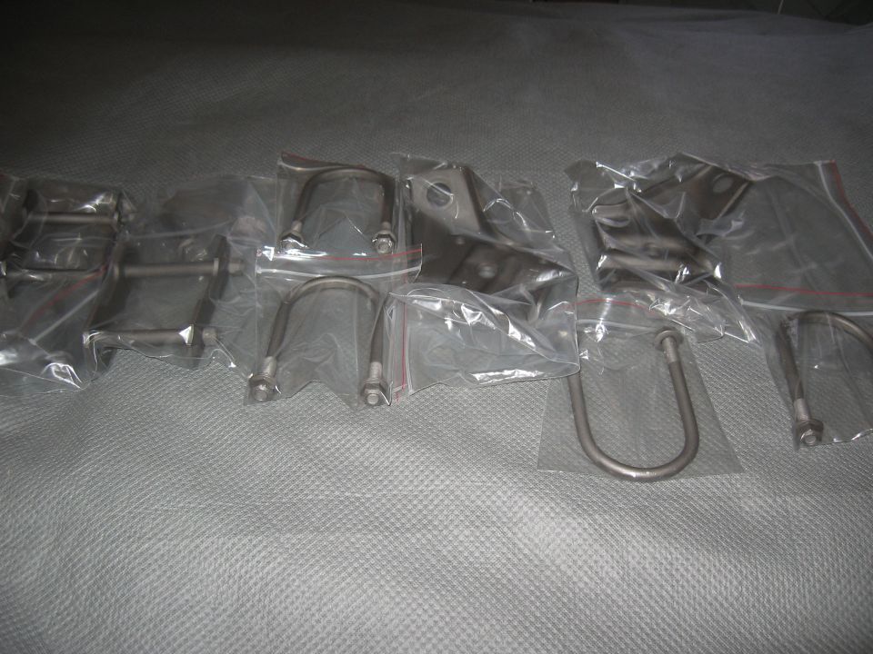 Several metal brackets and U-bolts are packaged in plastic bags on a gray surface