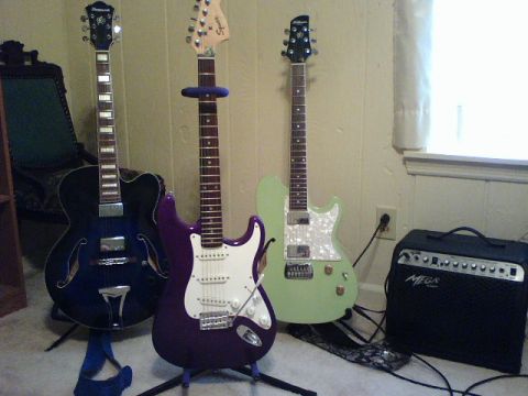 1995 Ford Bronco - Three electric guitars and a black amplifier are arranged on the floor near a wall and window.