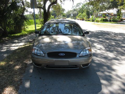 2002 Ford Taurus - A tan 2002 Ford Taurus is parked on the side of a residential street, with trees casting shadows.