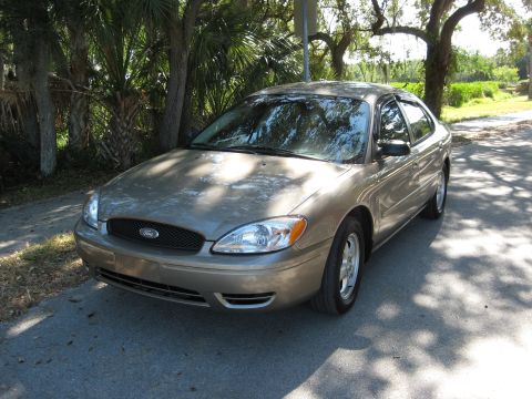 2002 Ford Taurus - A gold 2002 Ford Taurus sedan is parked on a road, with trees and foliage providing shade.