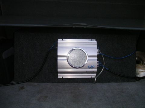1994 Ford Bronco - A silver car amplifier with a 620 WATT rating is installed next to a subwoofer in the trunk of a vehicle.
