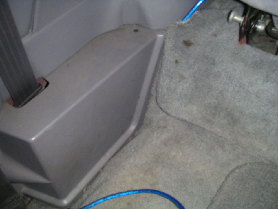 Vehicle interior showing gray carpet, a gray plastic trim piece, and a seatbelt mechanism