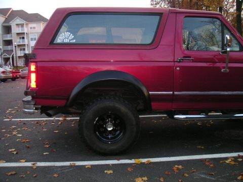 1994 Ford Bronco - Side profile of a red 1994 Ford Bronco parked in a lot with fallen leaves.