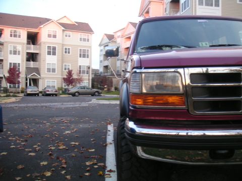 1994 Ford Bronco - Maroon Ford truck front view with chrome grille and amber turn signals, parked in a lot with apartment buildings in the background.